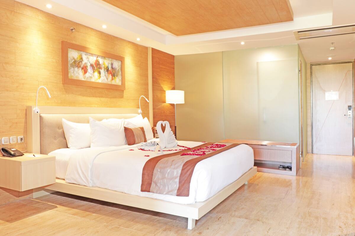 A modern hotel room with a large bed, a bedside table with a phone, a wall-mounted painting, and a nightstand.