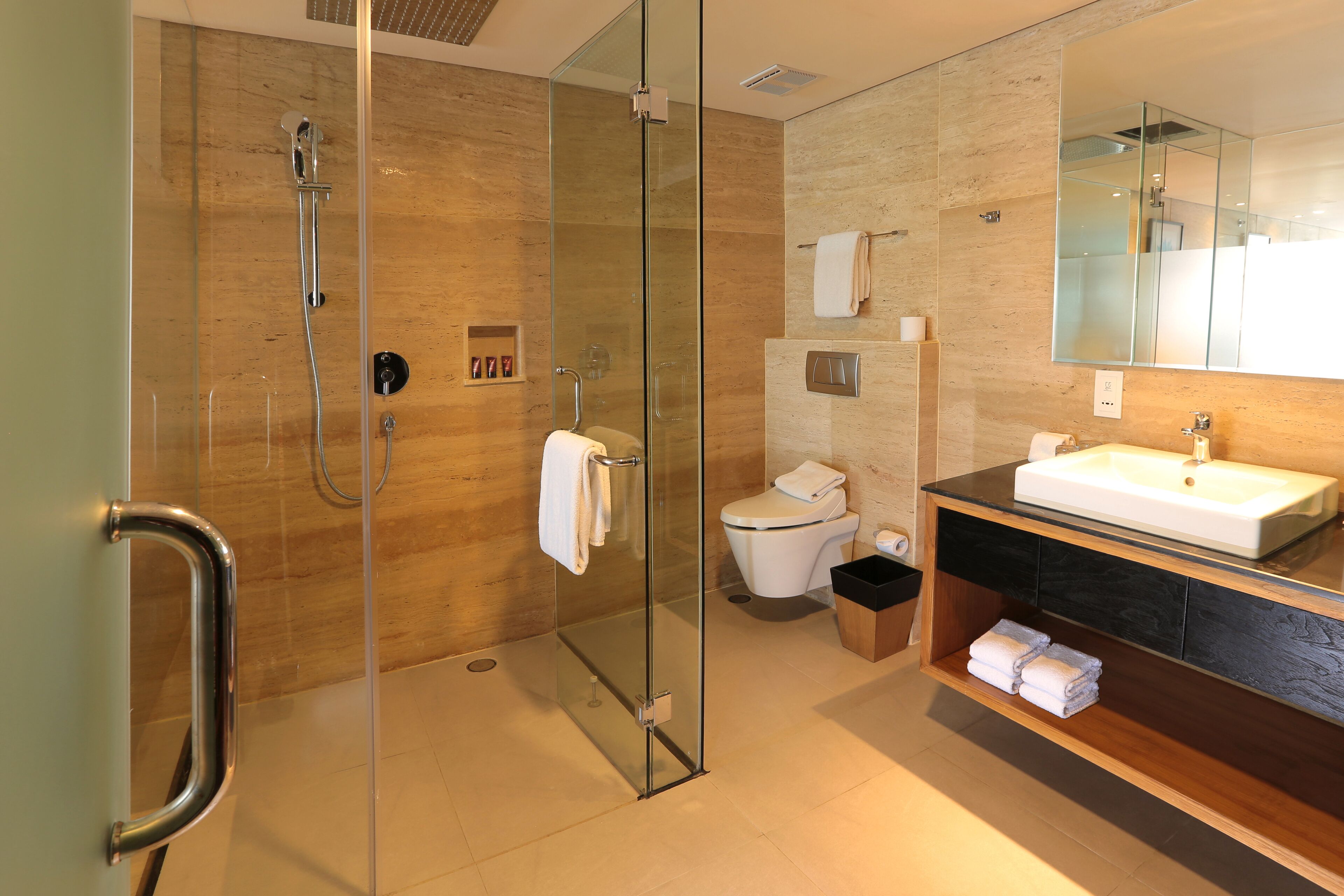 Un baño moderno con ducha envuelta en vidrio, inodoro, lavabo y tocador con estantes.
