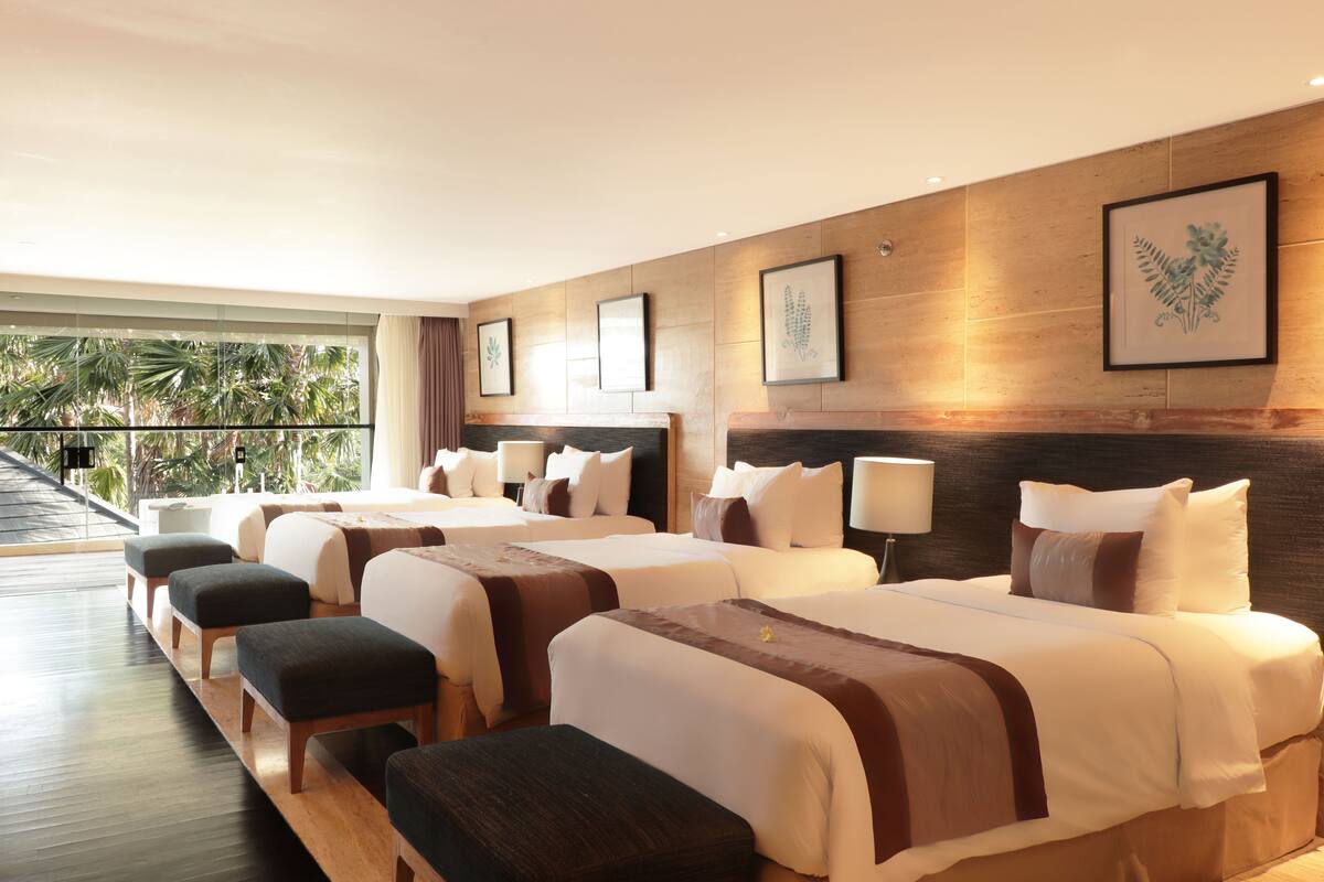 A hotel room with two beds, a wooden floor, and a balcony with a view of palm trees.