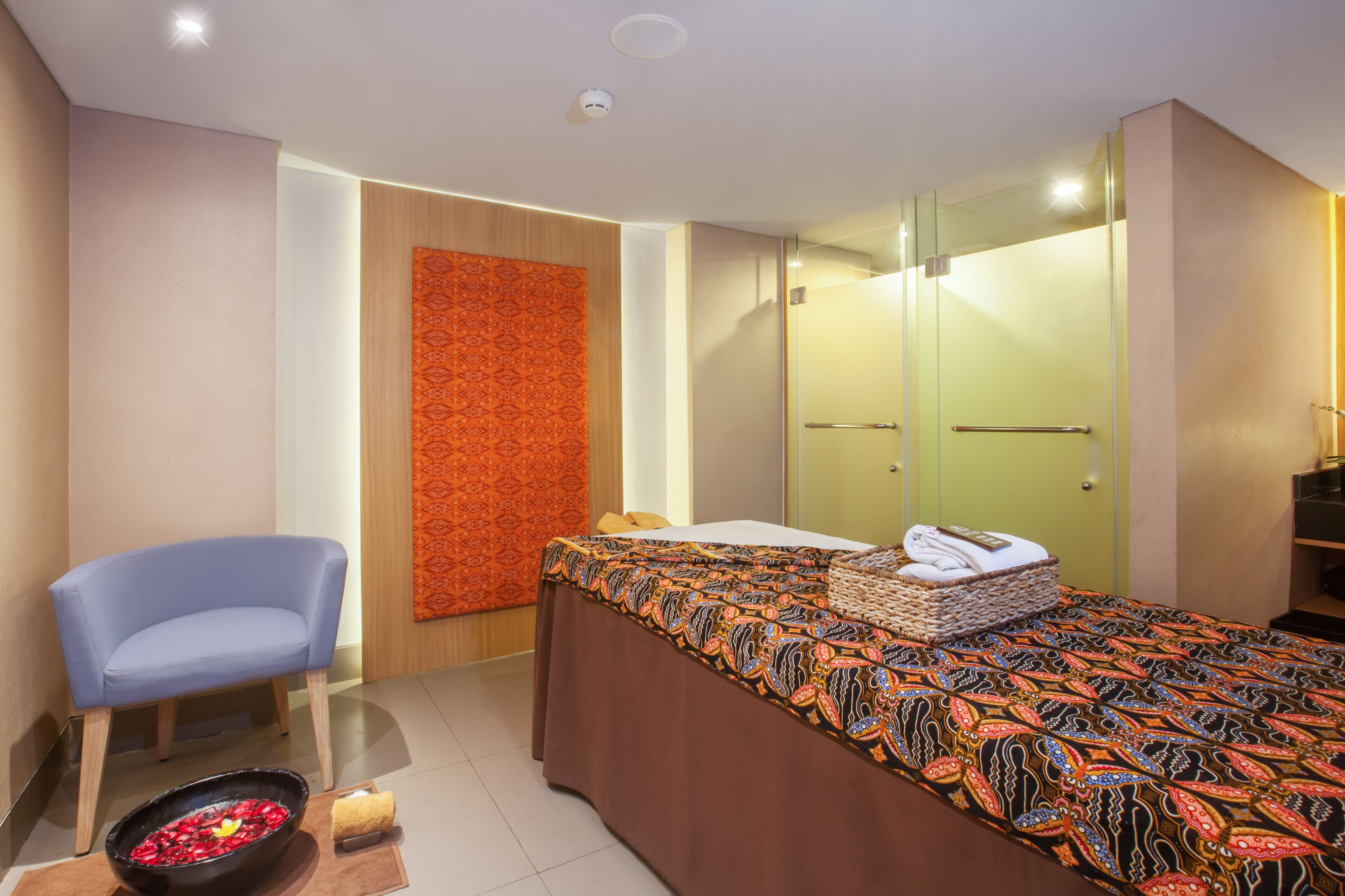 A modern room with a bed, a chair, a small table with towels, and a decorative wall.