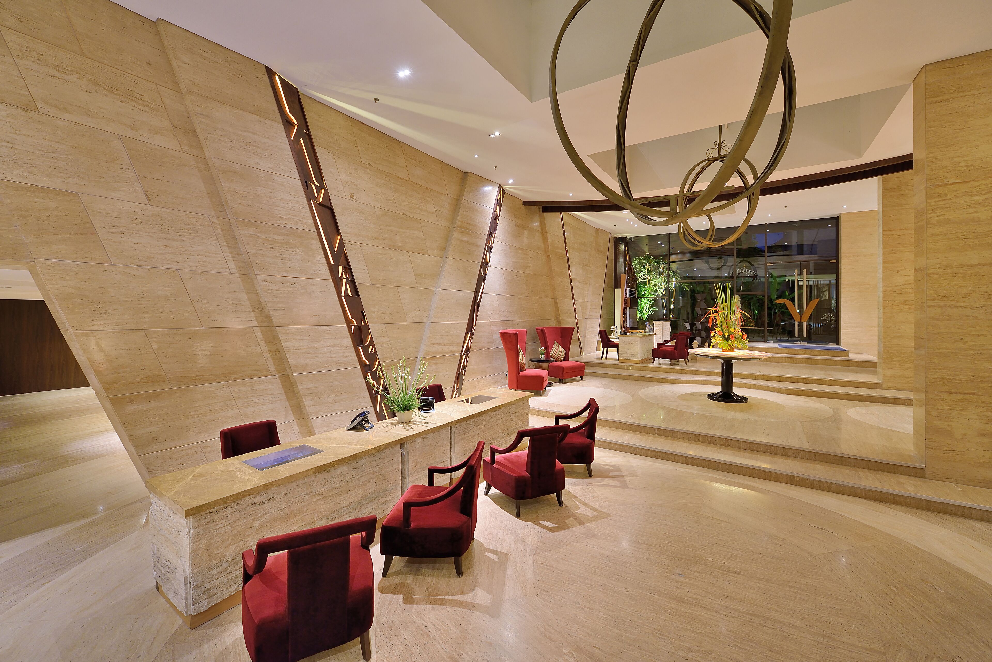 Un vestíbulo moderno con una mesa de recepción, sillas rojas y una planta decorativa.