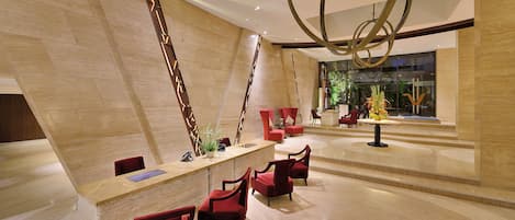 Un vestíbulo moderno con una mesa de recepción, sillas rojas y una planta decorativa.