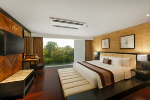 Relax in comfort with a large bed, flat-screen TV, and a view of lush greenery.