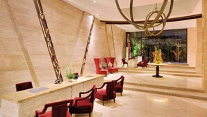 Un hall d’entrée spacieux doté d’un sol en marbre aux lignes courbes, de sièges rouges et d’un lustre moderne.