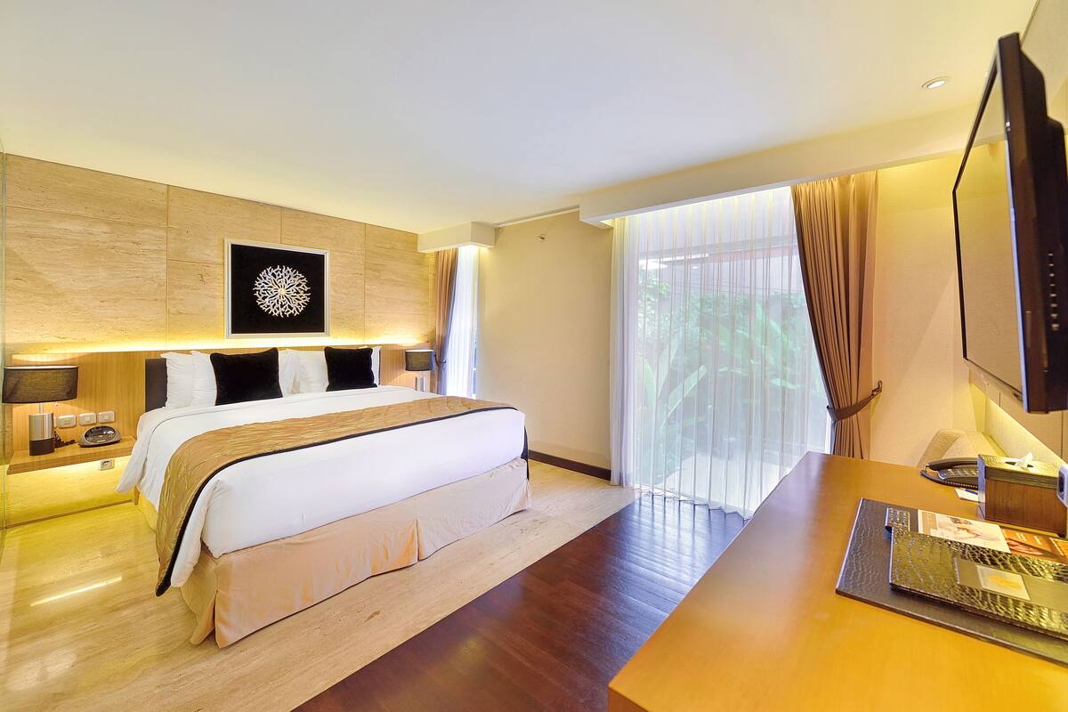 A modern hotel room with a large bed, bedside tables, a desk, and a TV.