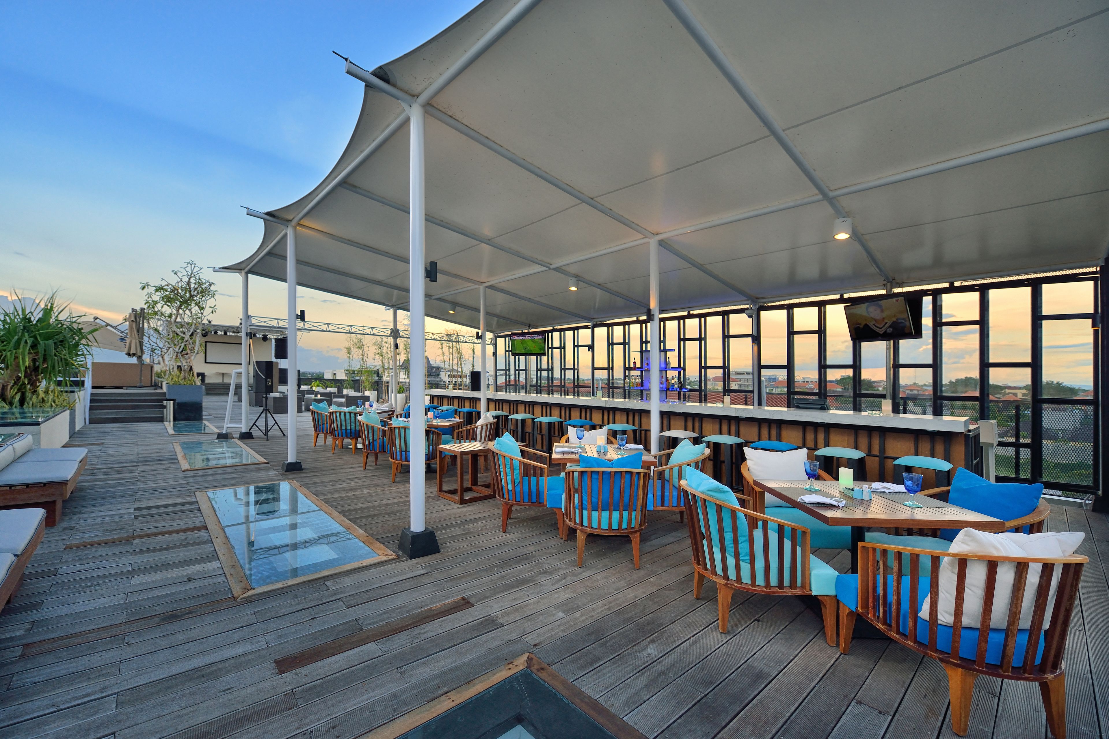 An outdoor seating area with wooden tables and chairs, a covered roof, and a view of the cityscape.