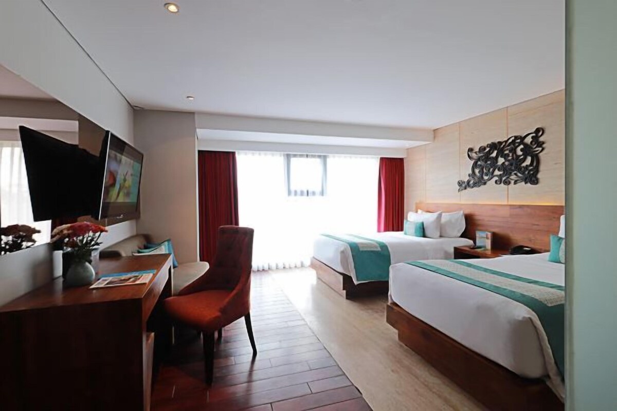 Habitación de hotel con dos camas, un escritorio, una silla, un televisor y una ventana con cortinas.