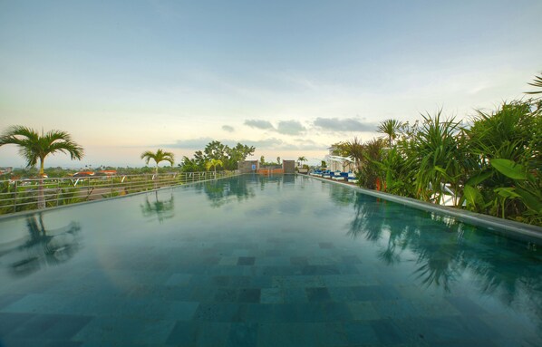 Relax by the serene pool surrounded by lush tropical plants and a clear blue water surface.