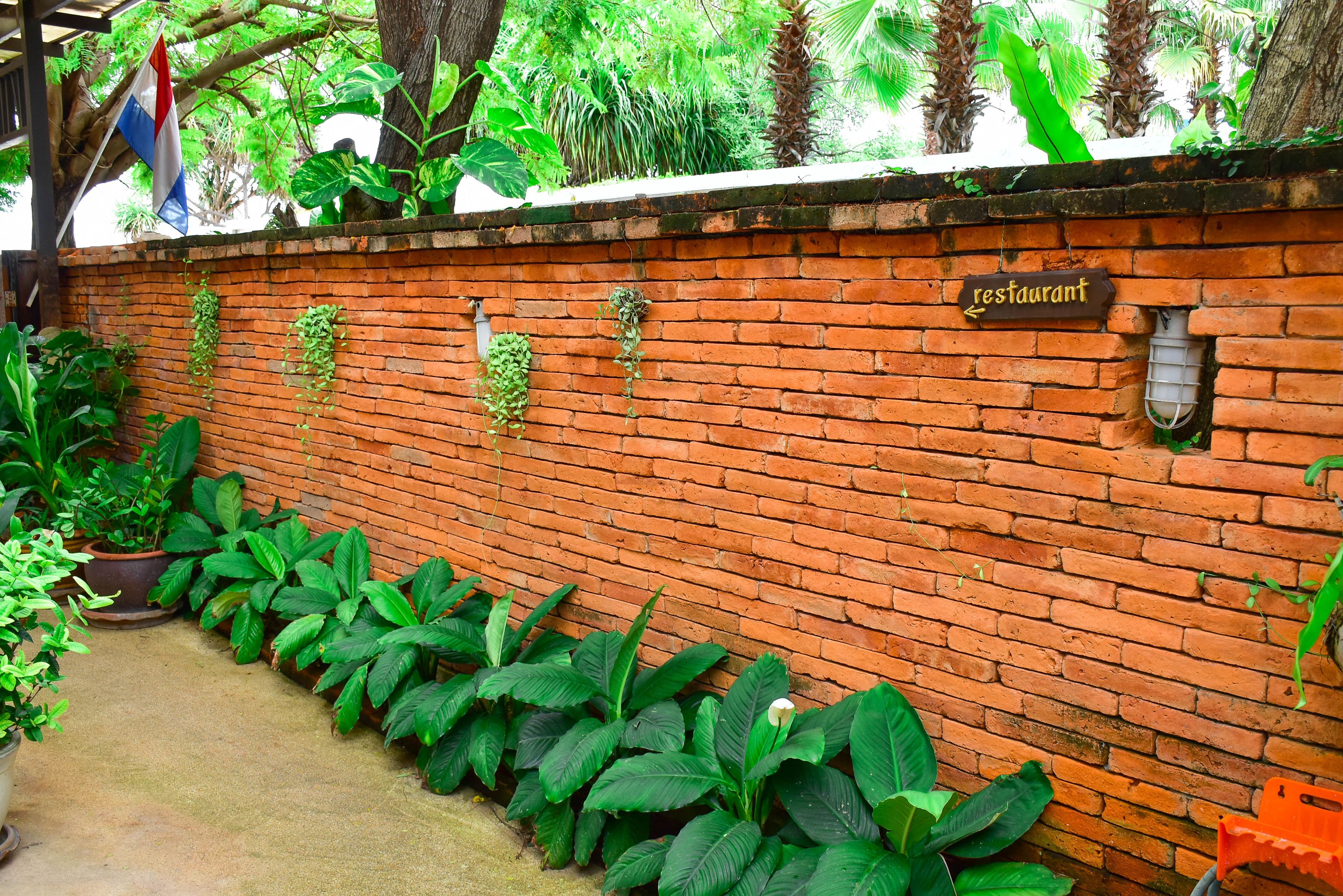 A brick wall with a restaurant sign, potted plants, and a concrete pathway.