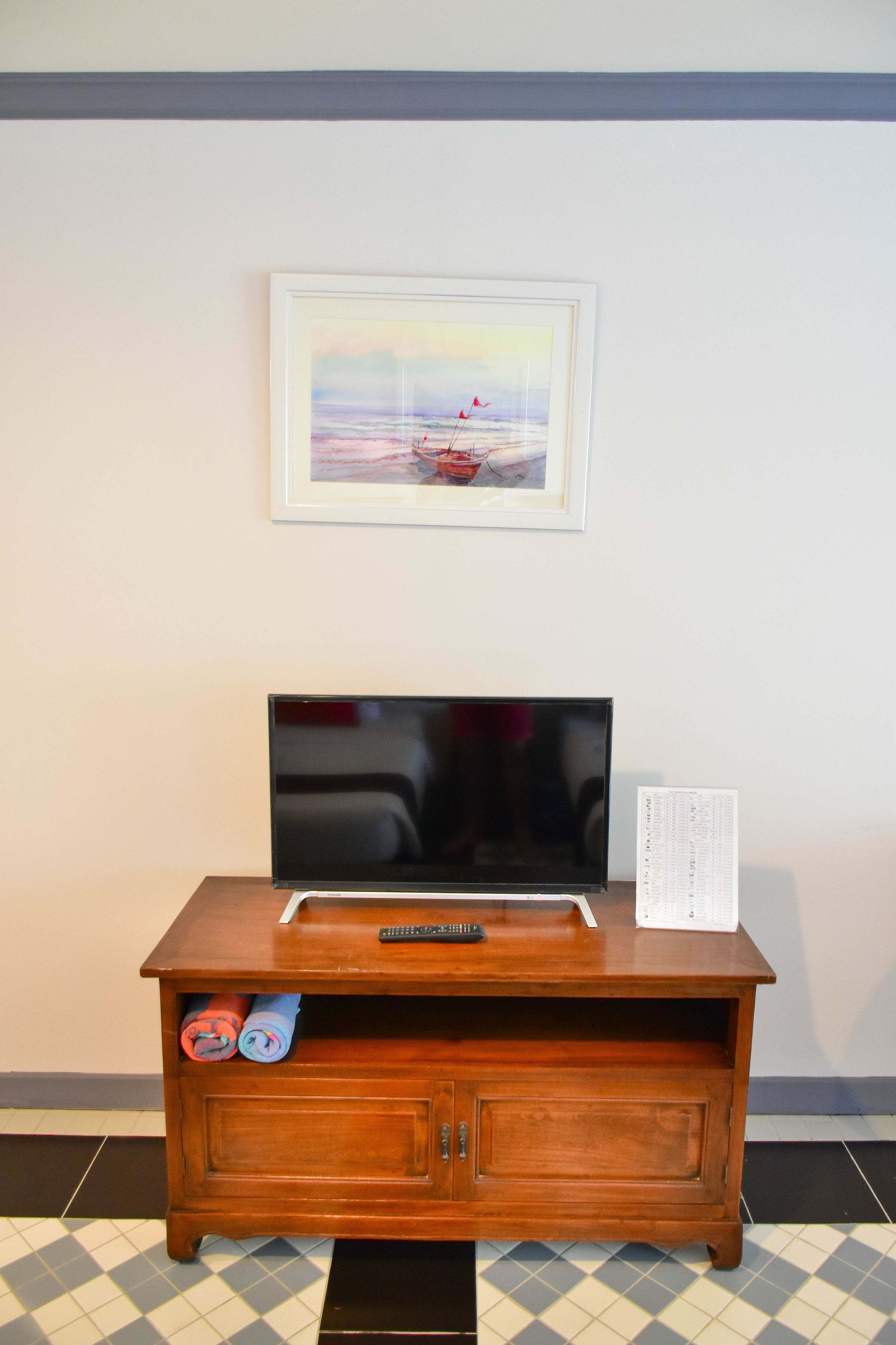 A wooden TV stand with a flat-screen TV, remote controls, and a framed picture on the wall above.