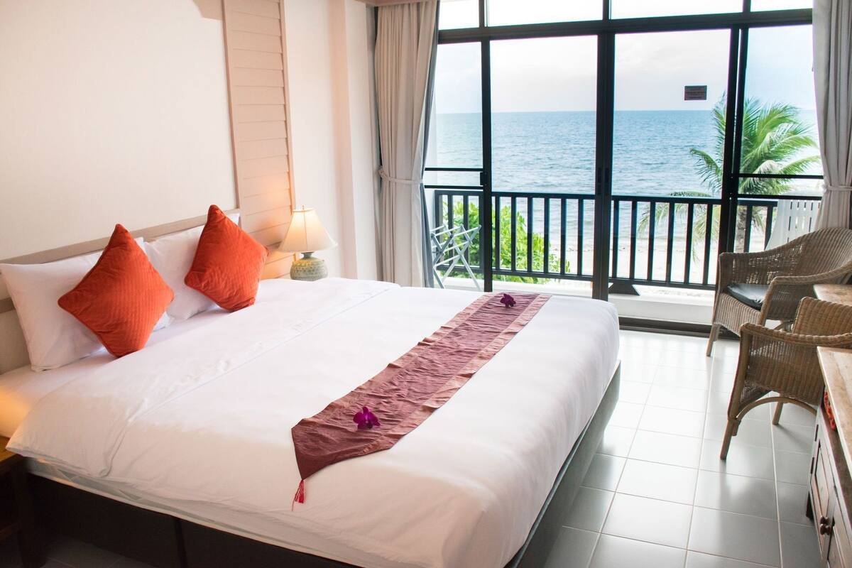Ein Hotelzimmer mit Bett, Nachttisch, Lampe, Stuhl und Meerblick.