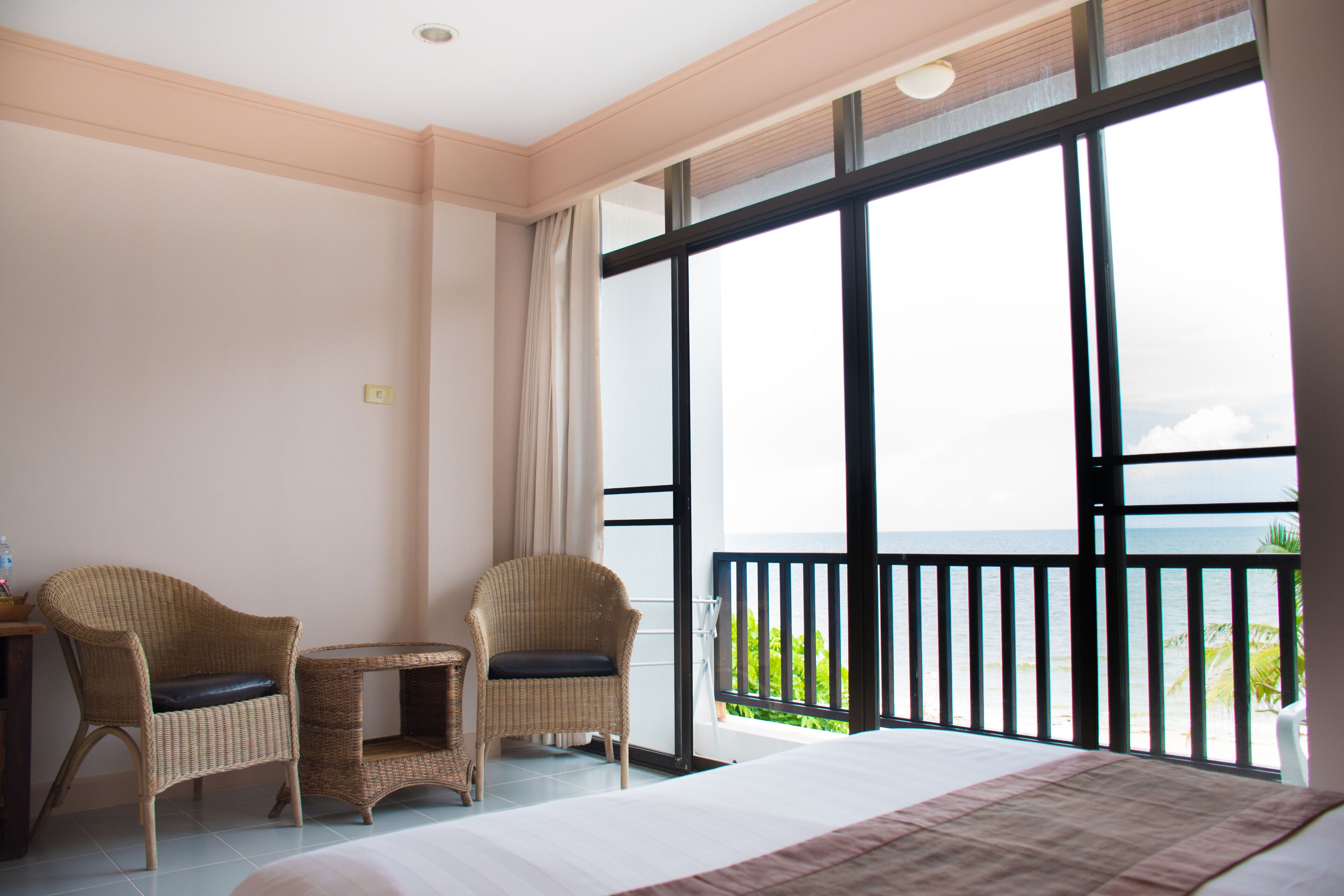 Habitación de hotel con una cama grande, dos sillas de mimbre, una mesita y un balcón con vista a la playa.