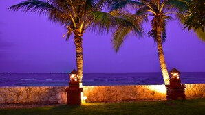 A stone wall with two palm trees and a view of the ocean at dusk. - Sea Memories White Sand Beach Hotel (Hua Hin)