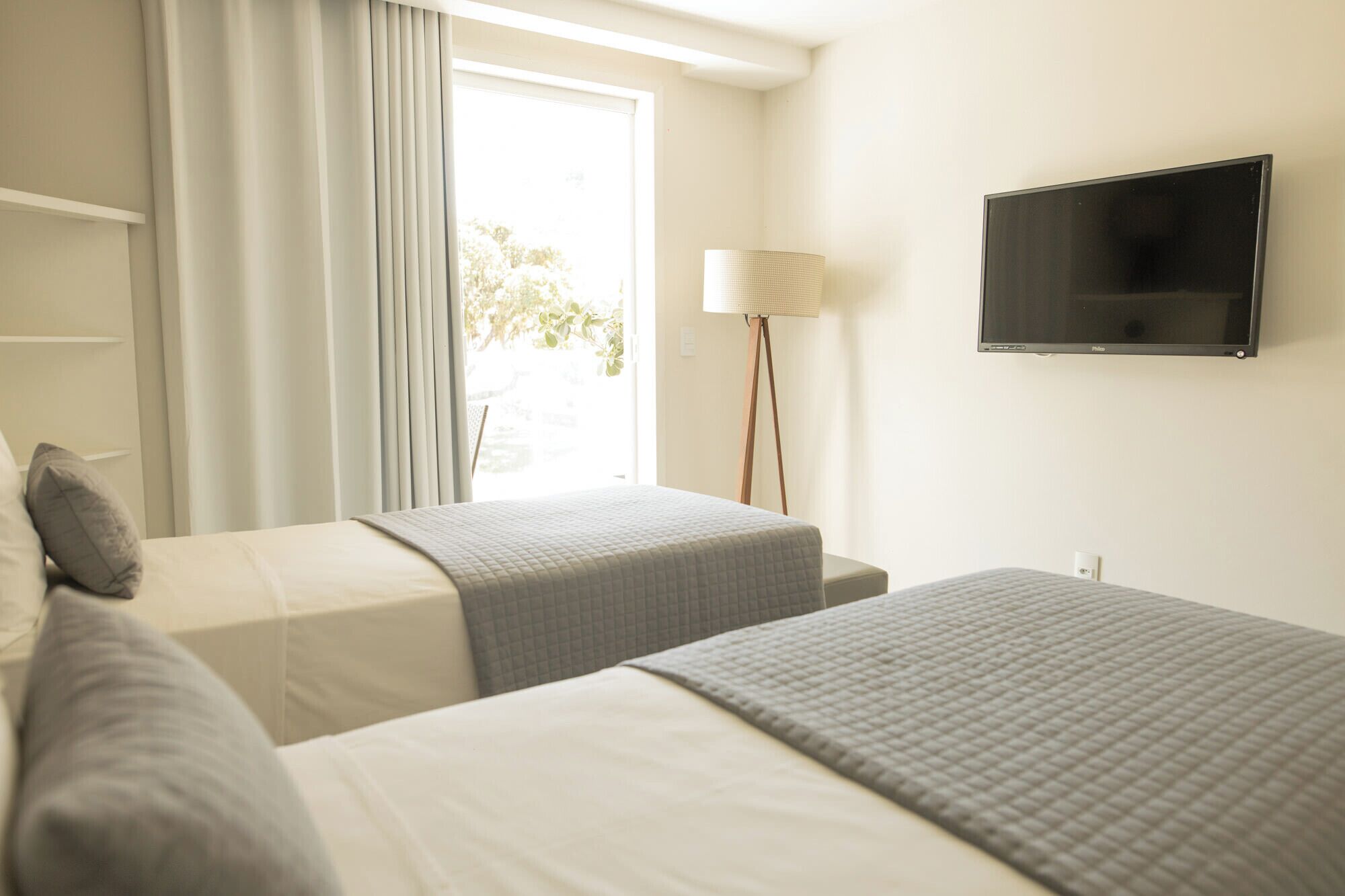 Ein Hotelzimmer mit zwei Betten, einem Fernseher, einer Lampe und einem Vorhangfenster.
