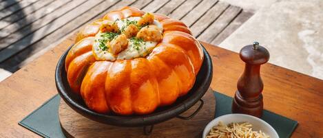 A bread bowl with shrimp and mashed potatoes, accompanied by a pepper grinder and bowls of rice and fries on a wooden table.