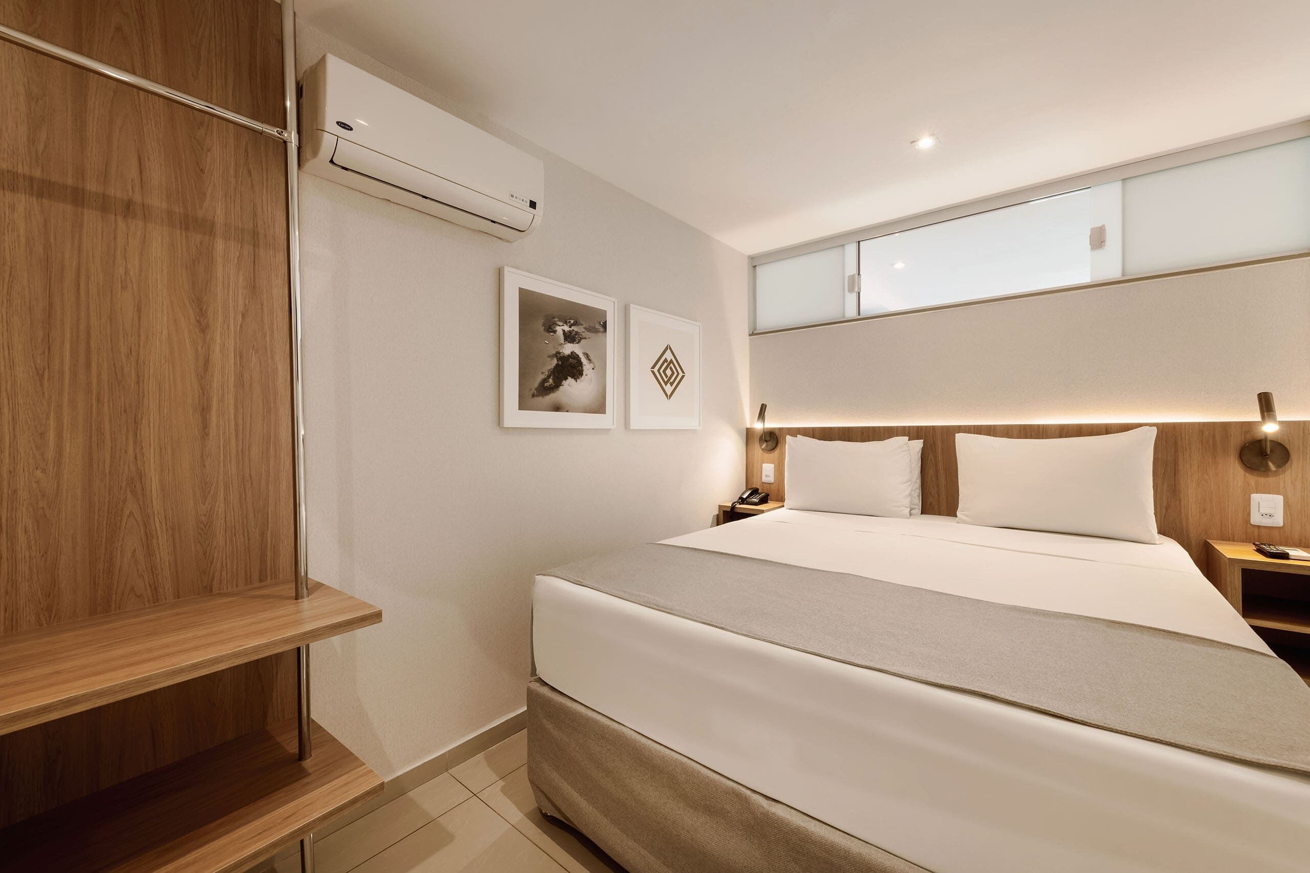 A modern hotel room with a large bed, wooden wardrobe, and a small bedside table.