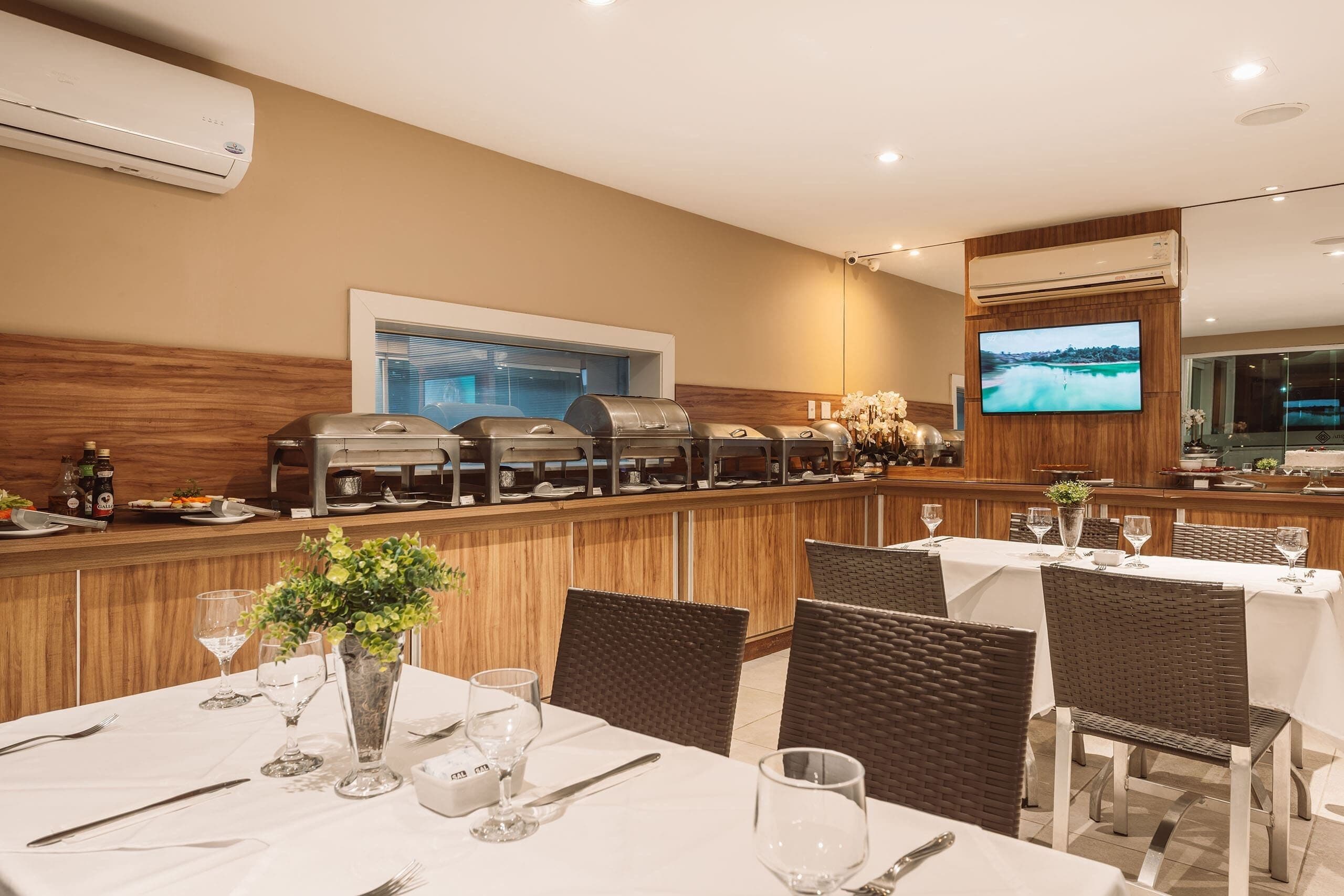 Un restaurante con zona de bar, varias mesas con sillas y una pantalla de televisión en la pared.