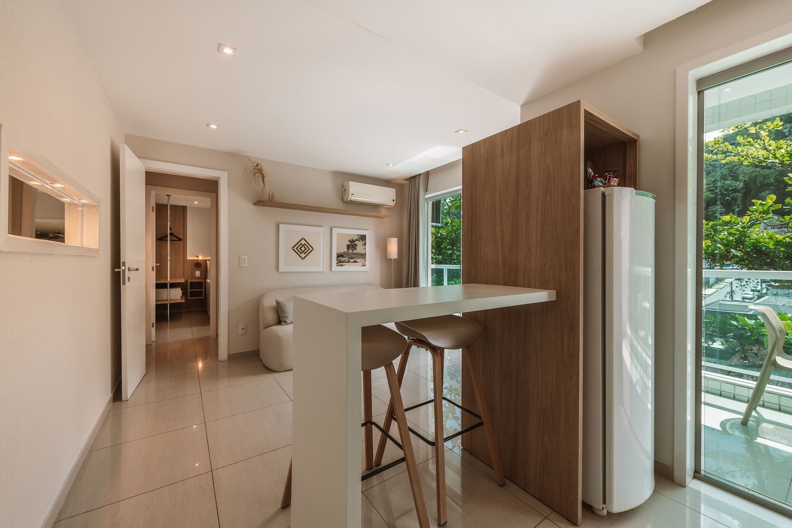 A modern kitchen with a bar area, a refrigerator, and a view of greenery outside.