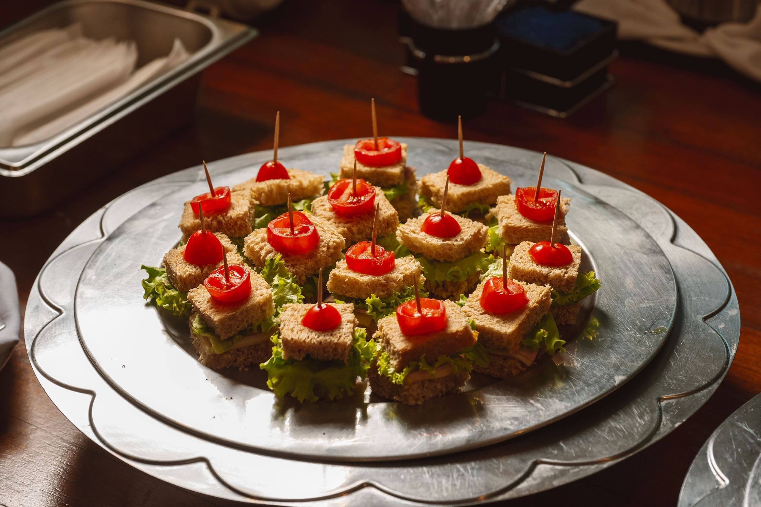 A tray of sandwiches with cherry tomatoes on a metal plate.
