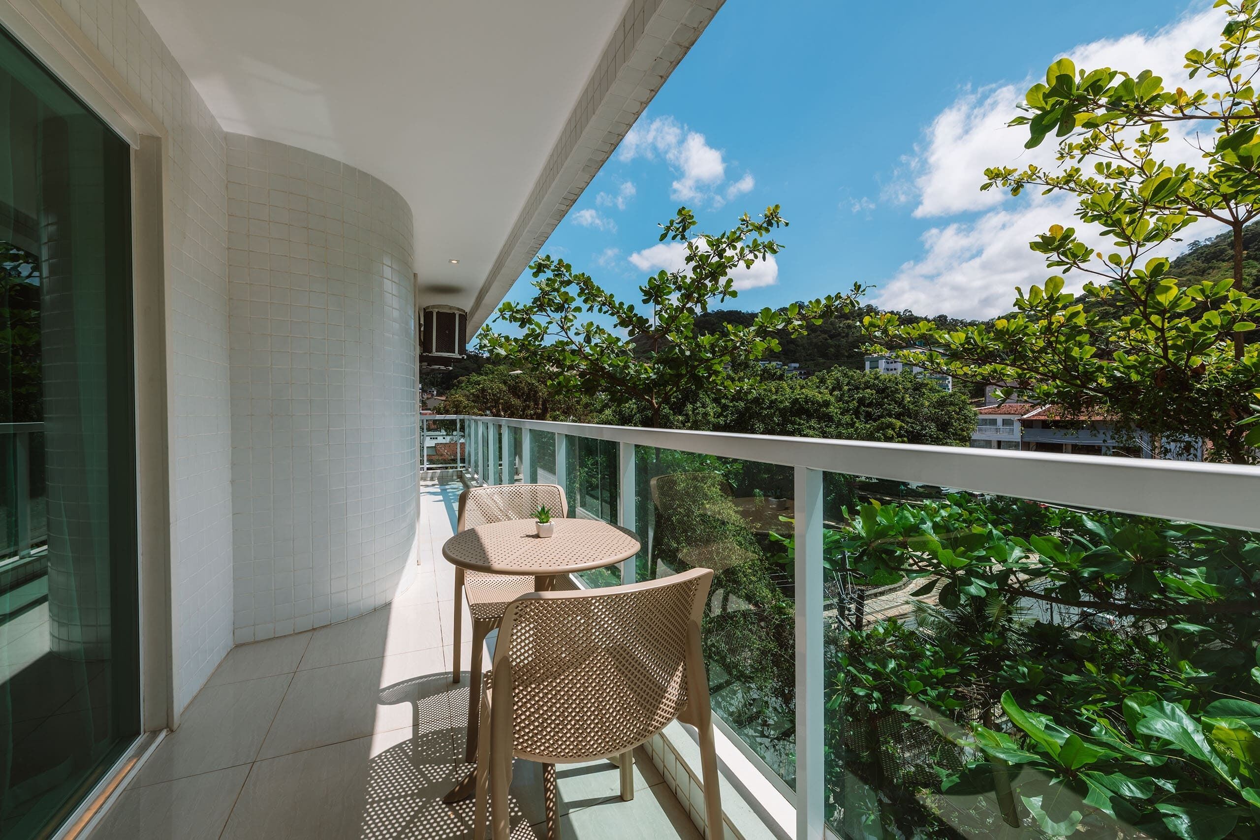 A balcony with a glass railing, a small table, and two wicker chairs.