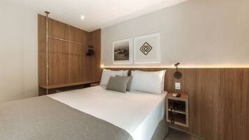 A modern hotel room with a large bed, a wooden wardrobe, a bedside table with a phone, and two framed pictures on the wall.