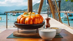 Una calabaza sobre un soporte con cuencos de arroz y un molinillo de pimienta en una mesa de madera cerca de la orilla.
