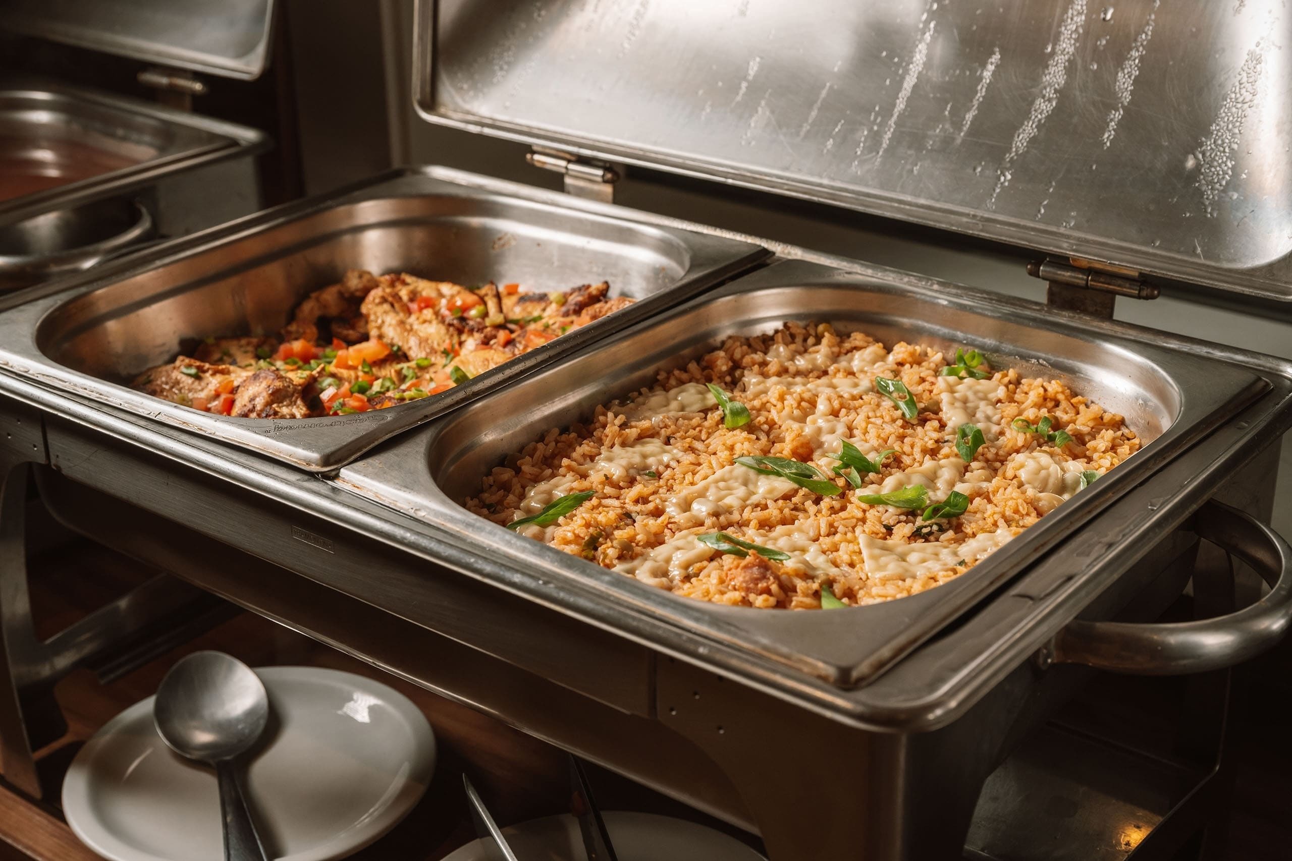 A buffet with two large metal serving trays, one containing a rice dish with vegetables and the other a meat dish.