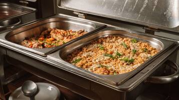 A buffet with two large metal serving trays, one containing a rice dish with vegetables and the other a meat dish.