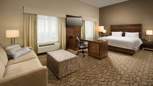 A hotel room with a bed, a desk, a chair, a sofa, and a carpeted floor.