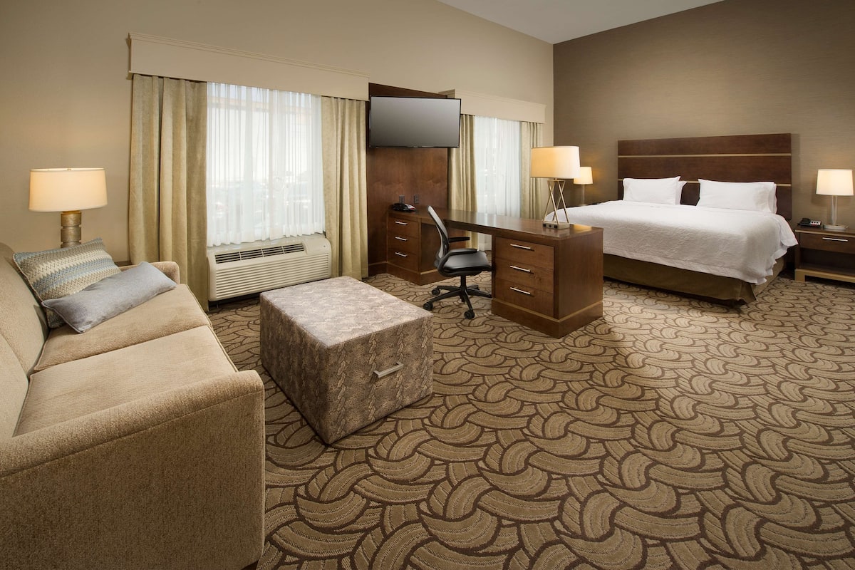 A hotel room with a bed, a desk, a chair, a sofa, and a carpeted floor.