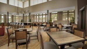 A spacious dining area with multiple tables and chairs, large windows, and hanging pendant lights.