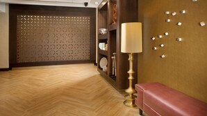 A hotel lobby with a wooden herringbone floor, a red bench, a lamp, and a decorative wall with geometric patterns.