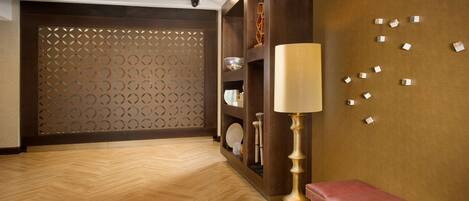 A hotel lobby with a wooden herringbone floor, a red bench, a lamp, and a decorative wall with geometric patterns.