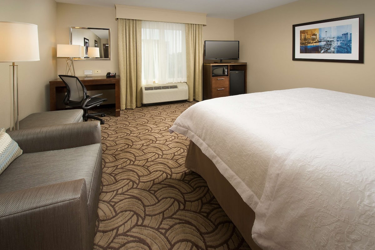 A hotel room with a bed, a desk with a chair, a television, and a heater.