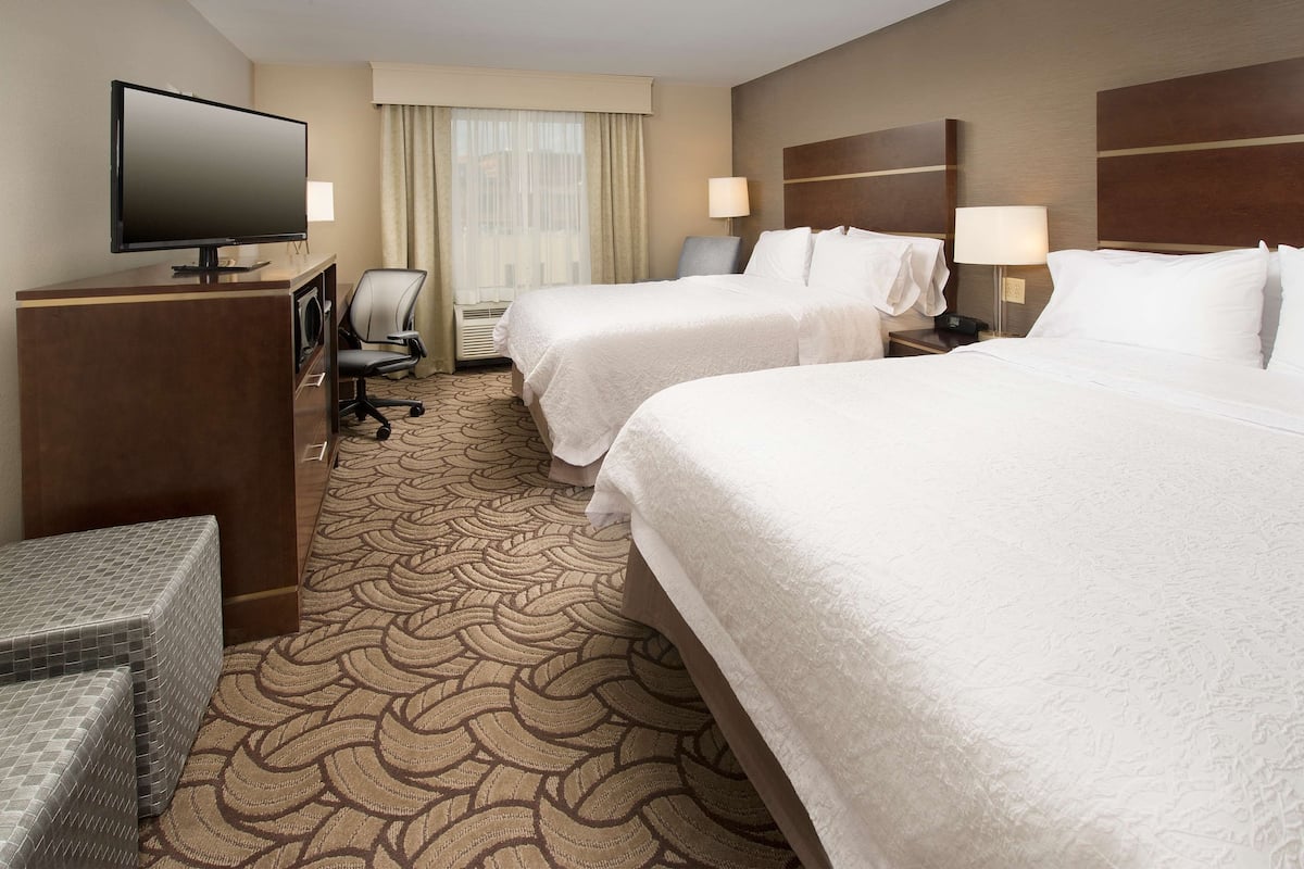 A hotel room with two beds, a desk with a flat-screen TV, a chair, and a small seating area.