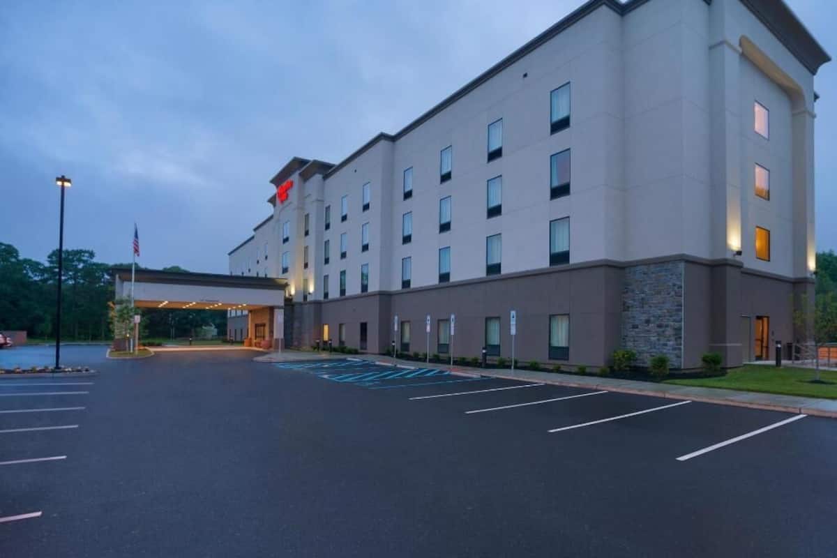 A multi-story hotel with a flat facade, a parking lot with marked spaces, and a flagpole with an American flag.