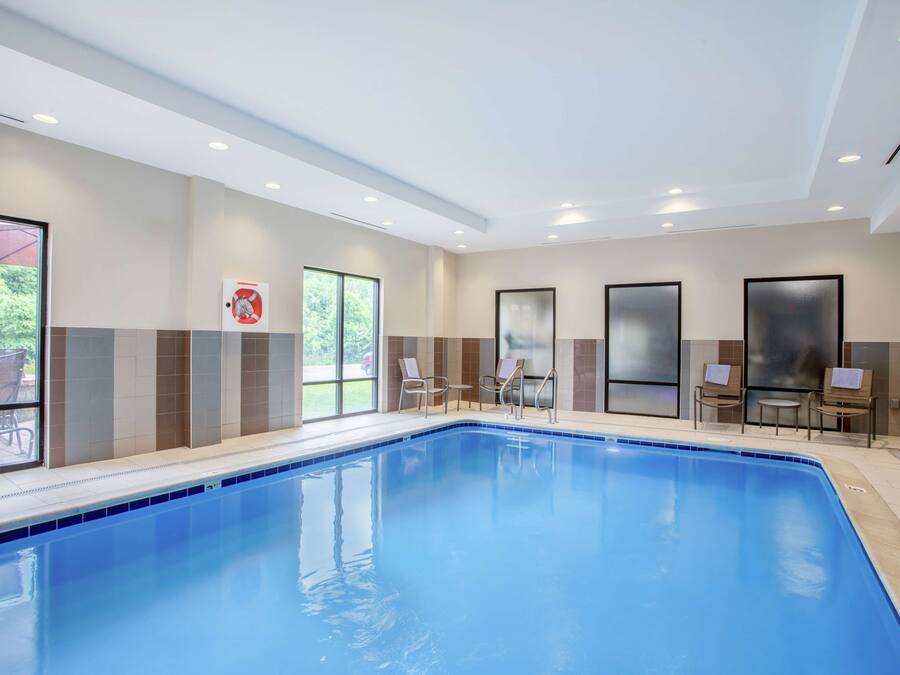A swimming pool with a tiled edge, surrounded by lounge chairs and a glass door leading to an outdoor area.