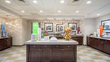 A hotel kitchen with a central island, various kitchen appliances, and a fruit display.