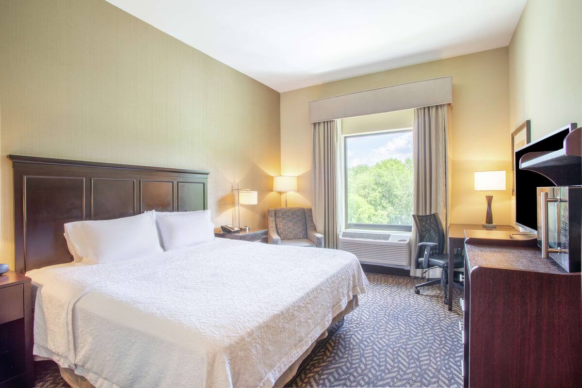 A hotel room with a large bed, a desk with a chair, a TV, and a window with curtains.