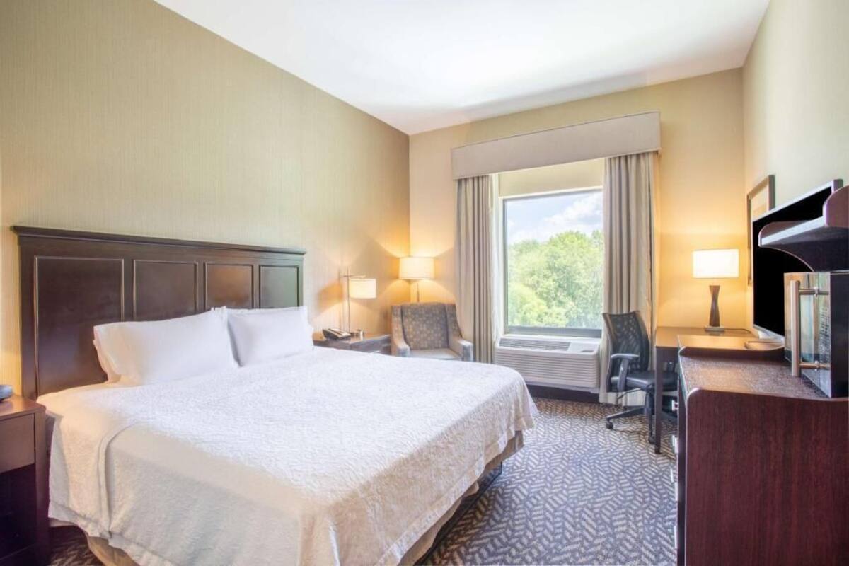 A hotel room with a large bed, a desk with a chair, a TV, and a window with curtains.