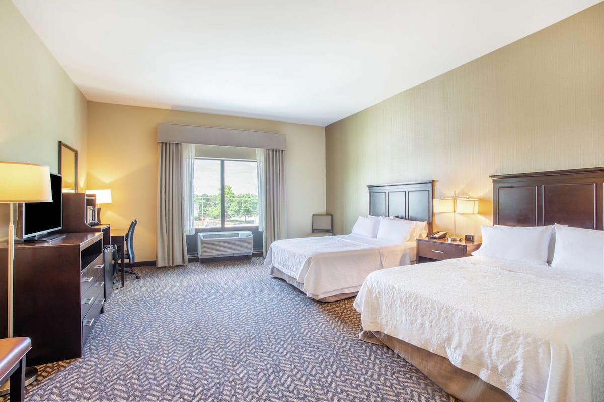 A hotel room with two beds, a desk with a TV, a chair, and a window with curtains.