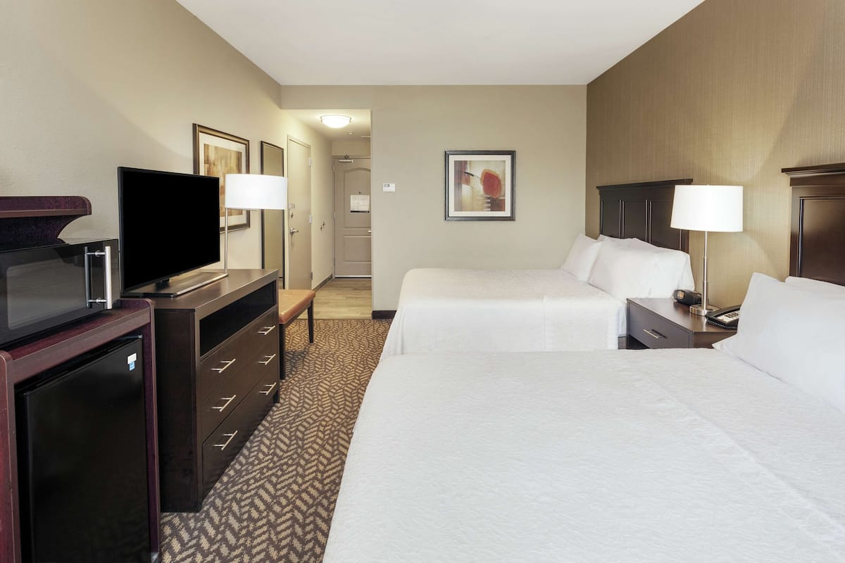 A hotel room with two beds, a television, a desk, and a dresser.