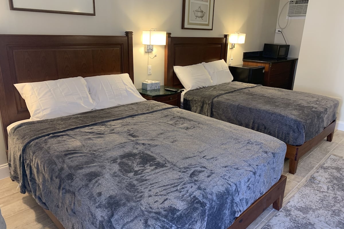 Hotellihuoneessa on kaksi sänkyä, joissa kummassakin on harmaa peitto ja valkoiset tyynyt. Sängyn vieressä on yöpöytälamput, yöpöytä, jossa on lamppu, ja televisio, joka on sijoitettu puupöydälle.
