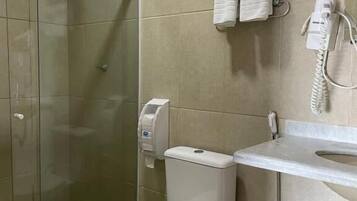 Une salle de bain avec une douche à parois de verre, des toilettes, un lavabo avec un porte-serviettes et un sèche-mains.