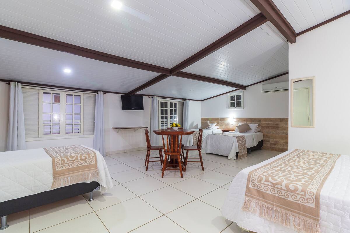 Una habitación de hotel con dos camas, una mesa de comedor con sillas, un televisor y una pequeña cocina.