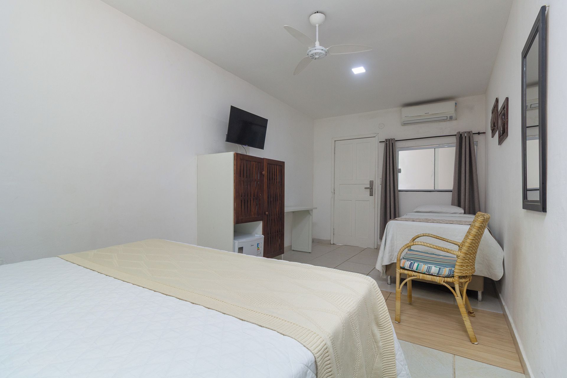 Un dormitorio con cama, una silla, un armario, televisor y aire acondicionado.