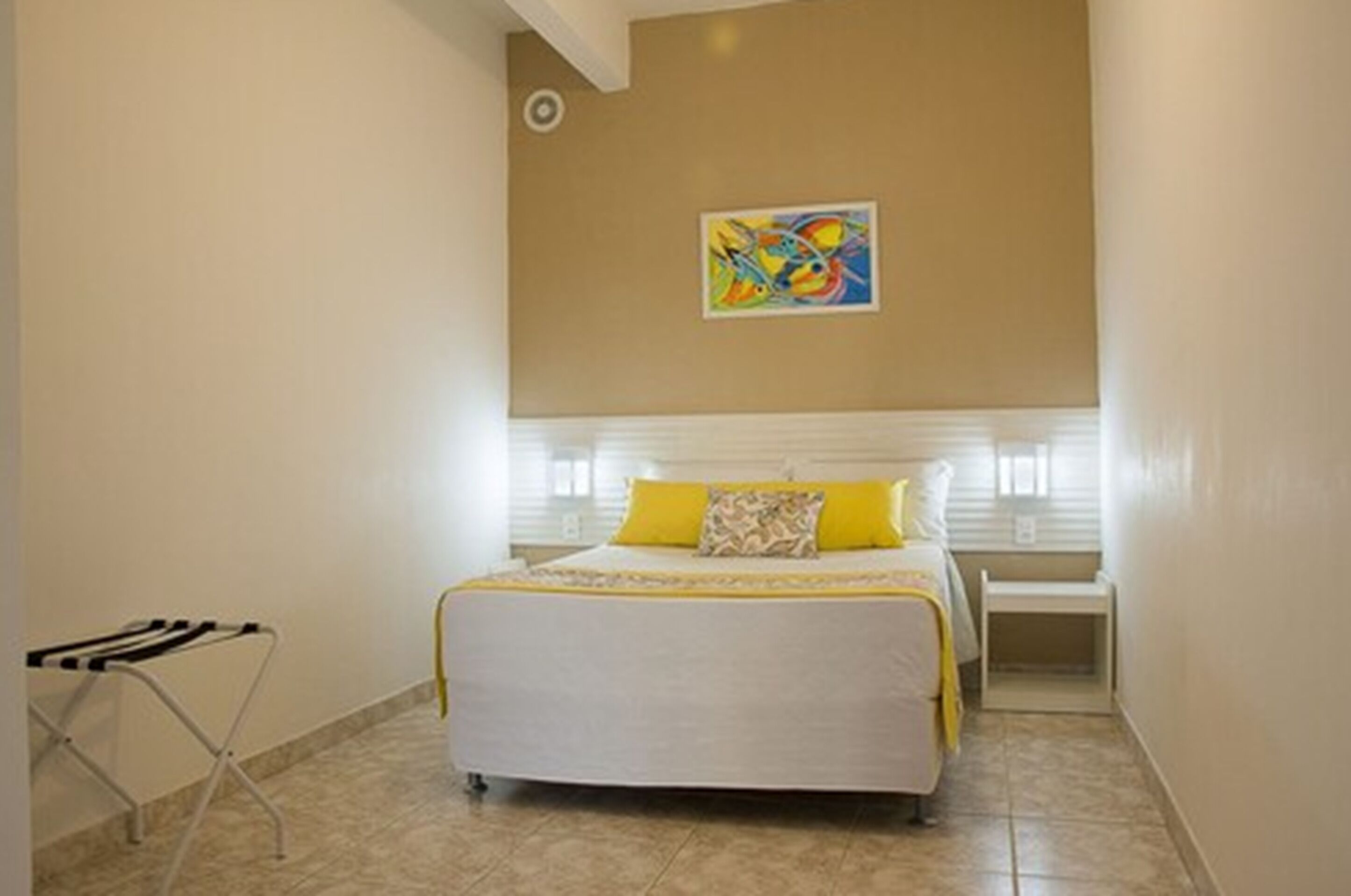 A bedroom with a bed, a colorful abstract painting on the wall, and a small table beside the bed.