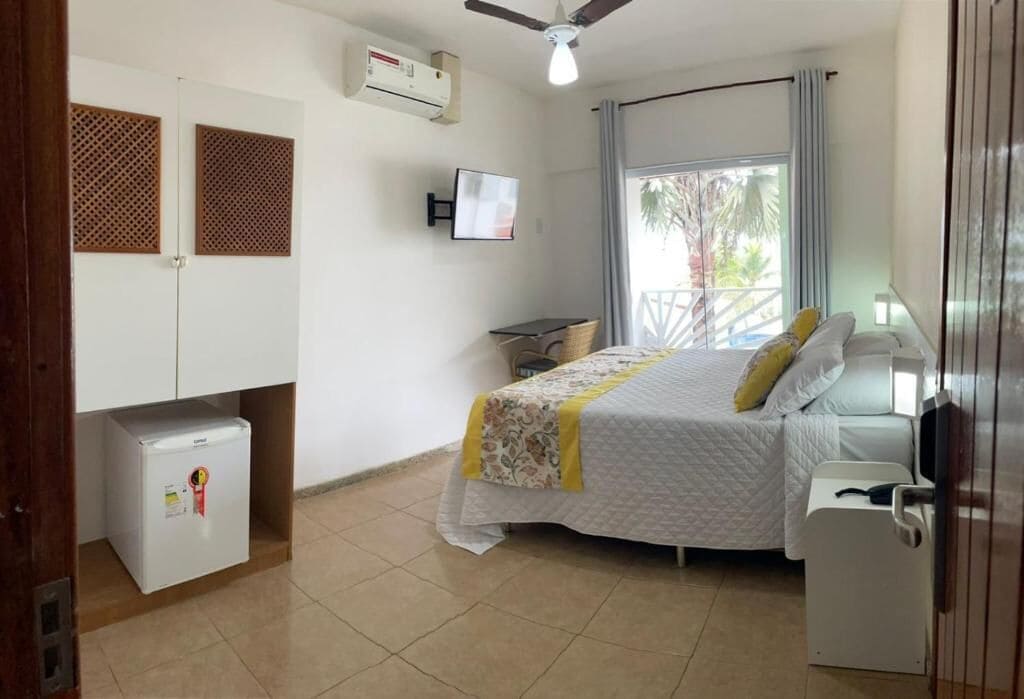 Un dormitorio con cama, un refrigerador pequeño, un televisor y un ventilador de techo.