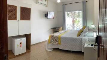Un dormitorio con cama, un refrigerador pequeño, un televisor y un ventilador de techo.