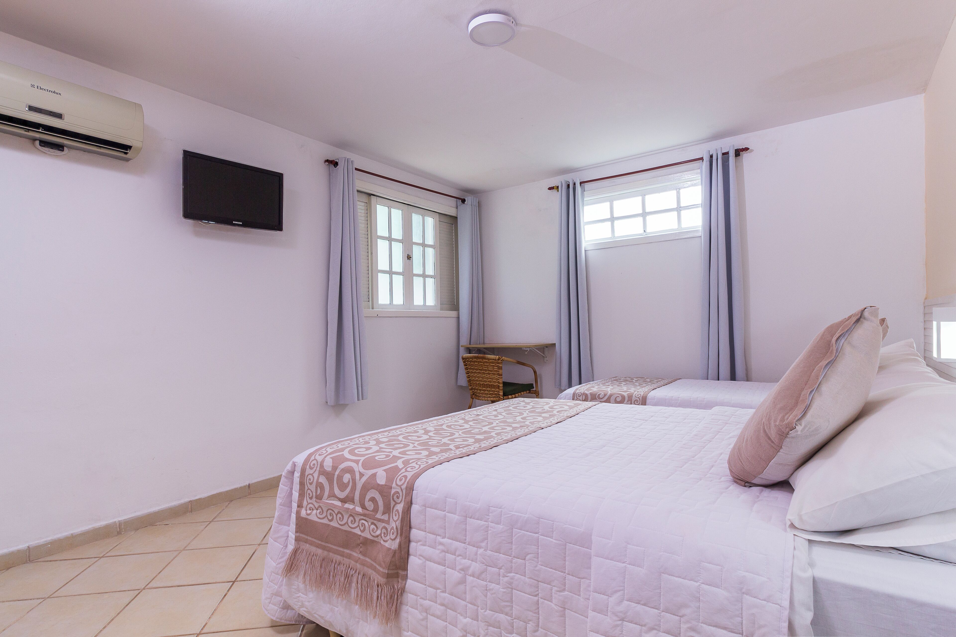 Slaapkamer met twee bedden, een flatscreen-tv, een airconditioner en een raam met gordijnen.